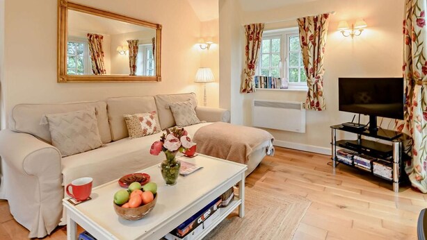 Een woonkamer met een bank, een salontafel met fruit en een vaas, een tv-meubel met een televisie, en een raam met gordijnen.