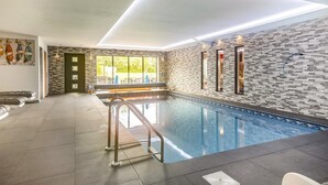 Ein moderner, überdachter Pool mit Steinwand, Glastür zum Außenbereich und Deckenbeleuchtung.