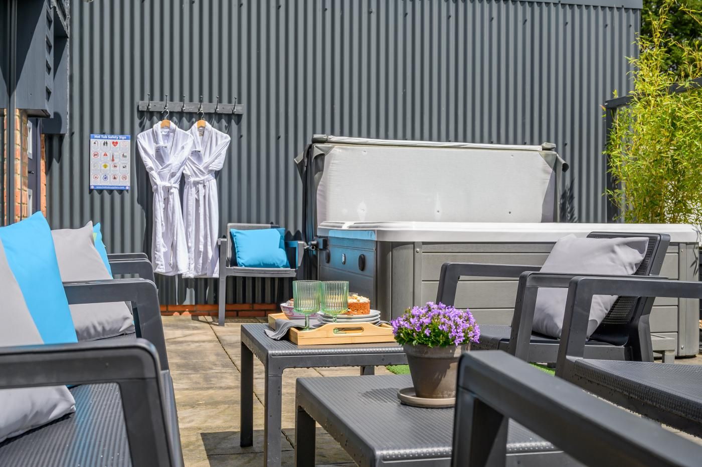 Een terras buiten met een barbecue, stoelen en een tafel met drankjes en gebak.