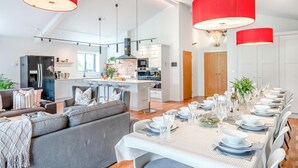 Eine moderne Küche mit einer zentralen Kochinsel, ein Essbereich mit einem langen Tisch für sechs Personen und ein Wohnbereich mit einer Couch und einem Couchtisch.