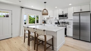 Une cuisine moderne avec des meubles blancs, des appareils en acier inoxydable et un grand îlot central doté de tabourets.