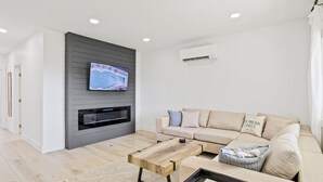 Un salon moderne avec un téléviseur à écran plat fixé au mur, un canapé beige, une table basse en bois et une cheminée.