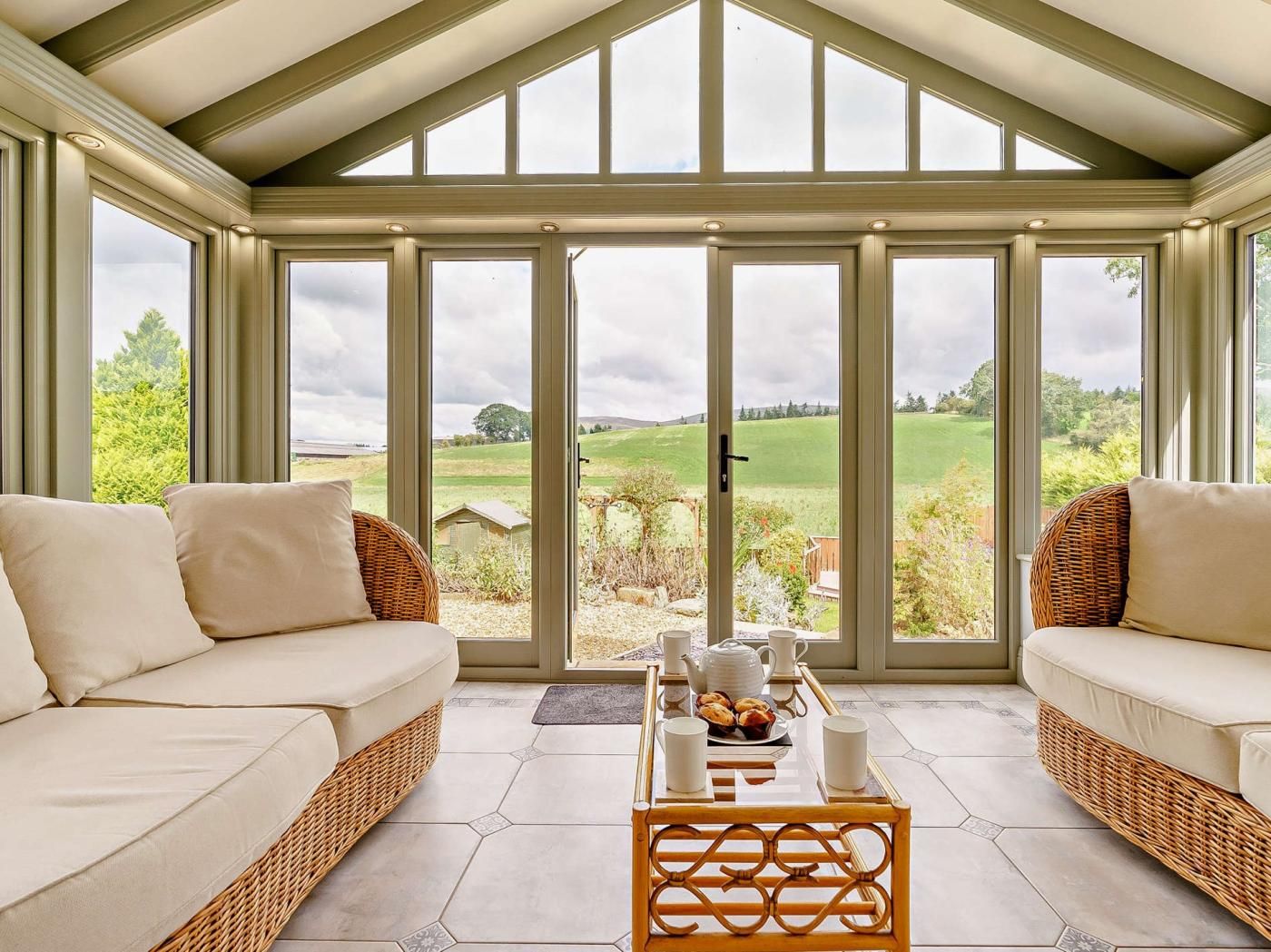 A conservatory with a view of a green landscape, furnished with two sofas and a coffee table.