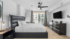 A modern bedroom with a large bed, a ceiling fan, a TV, and a view of buildings through the window. - Luxury Brickell With City Views & Rooftop Pool (Miami)