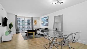A modern living room with a glass dining table, a sofa, a TV, and a large window. - Luxury Brickell With City Views & Rooftop Pool (Miami)