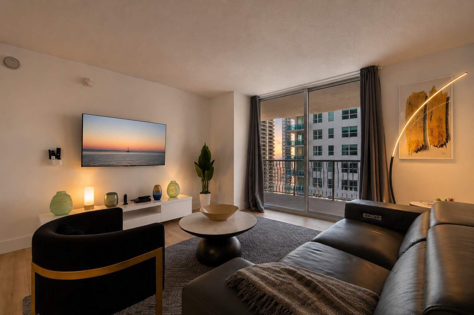 A modern living room with a large flat-screen TV, a sofa, a coffee table, and a view of a cityscape through a large window.