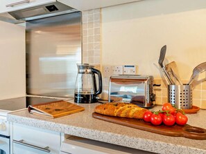 A kitchen with a stainless steel range hood, a Breville toaster, a coffee maker, a wooden cutting board, a loaf of bread, and a wooden cutting board with tomatoes. - 3 Bed in Haverfordwest (oc-92675) (Solva)