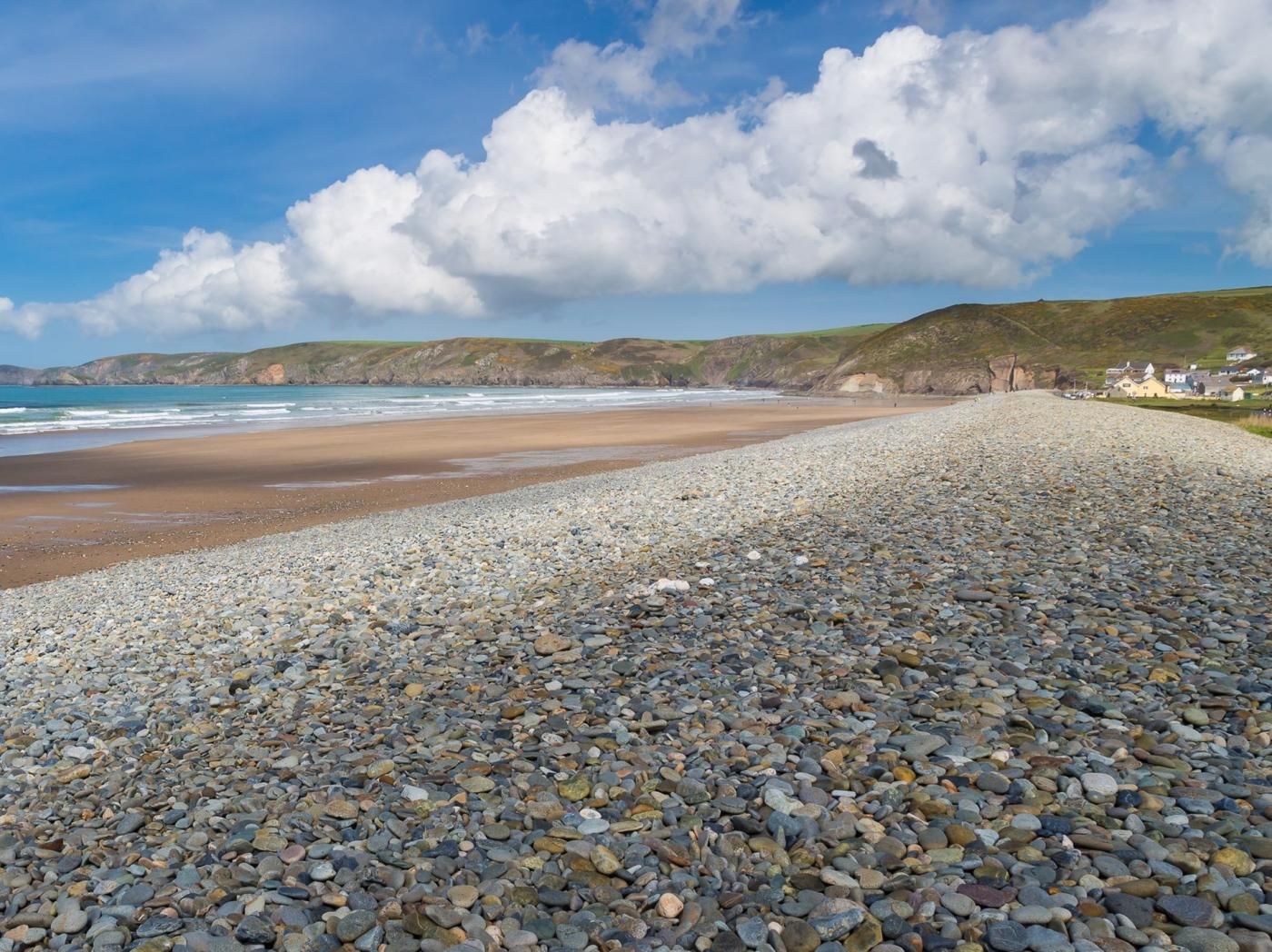 A pebbled beach with a view of the ocean and distant hills.