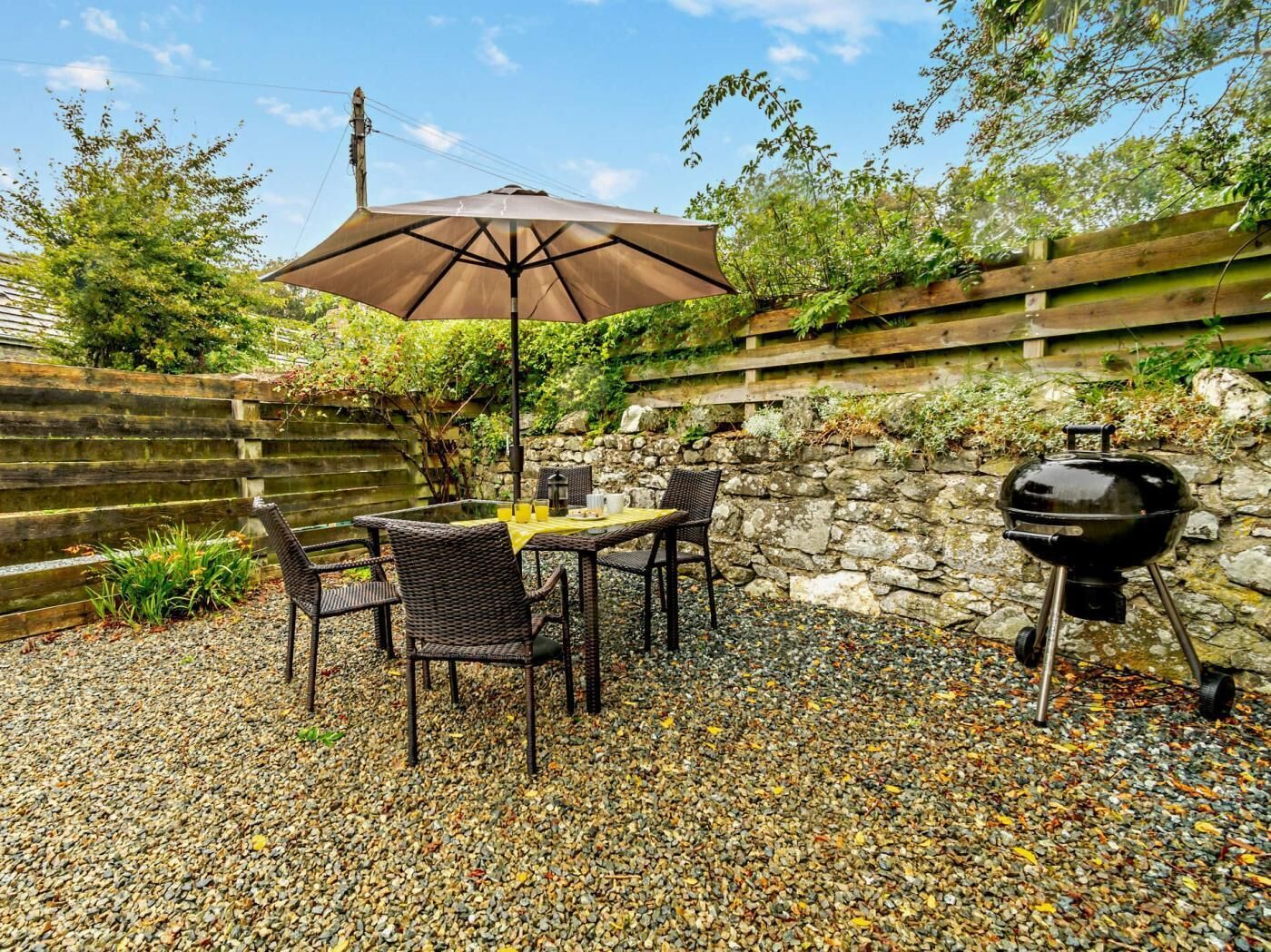 Een terras buiten met een tafel, stoelen, een barbecue en een stenen muur.