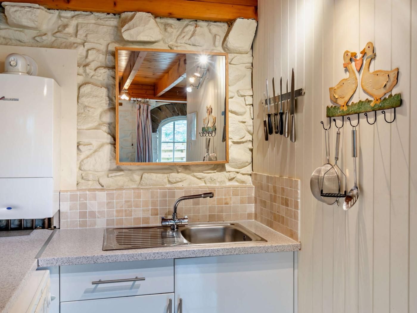 A kitchen with a stone wall, a sink, and a mirror above it.