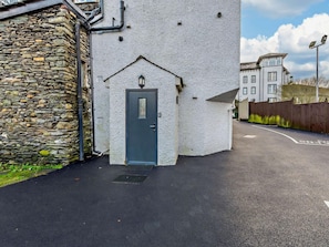A narrow street with a stone wall on one side and a white building with a dark door. - 1 Bed in Windermere (oc-93087) (Bowness on Windermere)
