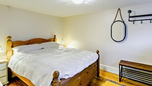 Une chambre à coucher avec un lit en bois, des lampes de chevet, un luminaire au plafond, un miroir fixé au mur et un banc.