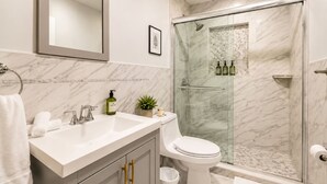 A bathroom with a marble sink, a toilet, a glass-enclosed shower, and a mirror above the sink. - Design District suite with free parking, centrally located. (Miami)