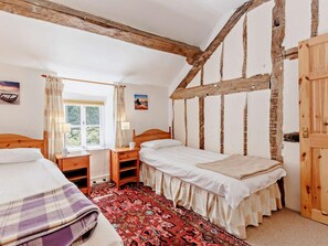 Ein Zimmer mit zwei Betten, einem fensterförmigen Vorhang, einem Holztisch und einem roten Teppich mit Muster.