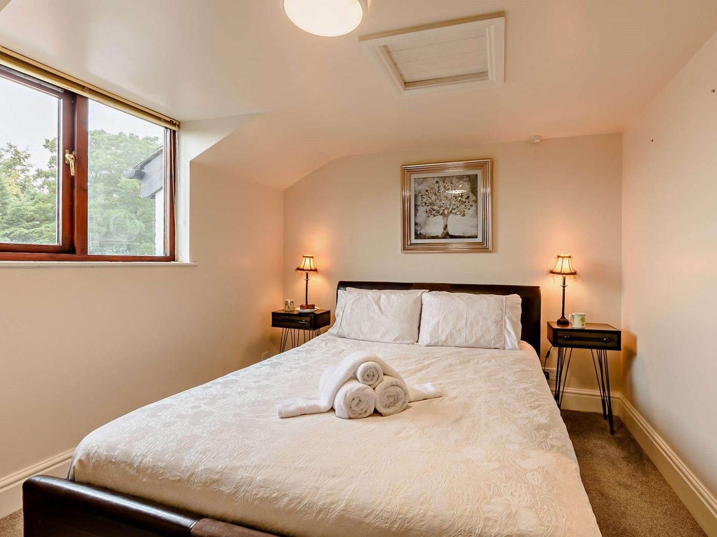 A bedroom with a bed, two bedside tables, a window, and a ceiling light.