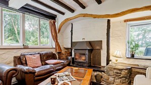 A cozy living room with a stone fireplace, leather sofa, and a coffee table with a newspaper. - 3 Bed in Machynlleth (oc-93083) (Cwm-Llinau)