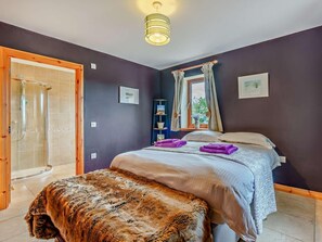 Een slaapkamer met een bed, een bankje, een douche, een raam met gordijnen en een plafondlamp.
