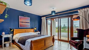 Ein Schlafzimmer mit einem Bett, Nachttischen, einem Schreibtisch, einem Stuhl, einem großen Fenster und Blick ins Freie.