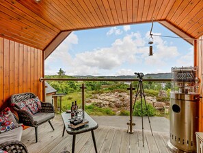 Een houten terras met uitzicht op een bergachtig landschap, een telescoop en een draagbare heater.