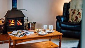 A cozy living room with a wood-burning stove, a leather sofa, and a coffee table with magazines and a sandwich. - 2 Bed in Machynlleth (oc-93079) (Cwm-Llinau)