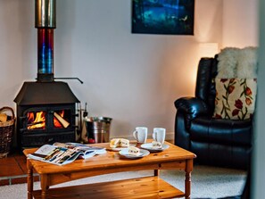 Ein gemütliches Wohnzimmer mit Kaminofen, einer Ledersofa und einem Couchtisch mit Zeitschriften und einem Sandwich.