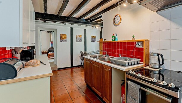 A kitchen with a central island, a stove, and a sink. There is a wooden ceiling and a red tiled backsplash. - 2 Bed in Machynlleth (oc-93079) (Cwm-Llinau)