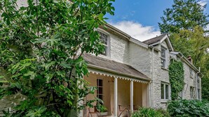 A two-story house with a porch, surrounded by lush greenery. - 2 Bed in Machynlleth (oc-93079) (Cwm-Llinau)