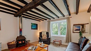 A cozy living room with a fireplace, a leather sofa, a wooden coffee table, and a large window with a view of greenery. - 2 Bed in Machynlleth (oc-93079) (Cwm-Llinau)