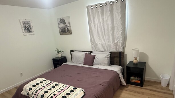 Une chambre à coucher comprenant un lit, des tables de chevet, une table de nuit, un rideau et deux tableaux accrochés au mur.