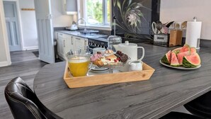 A breakfast tray with pastries, a jug of orange juice, and watermelon slices on a dark wooden table in a modern kitchen with a stove, cabinets, and a window. - 3 Bed in Keswick (oc-93202) (Keswick)