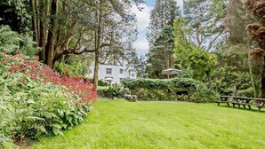 A well-maintained garden with a lawn, a stone wall, and a large white building in the background. - 1 Bed in Machynlleth (oc-93081) (Cwm-Llinau)