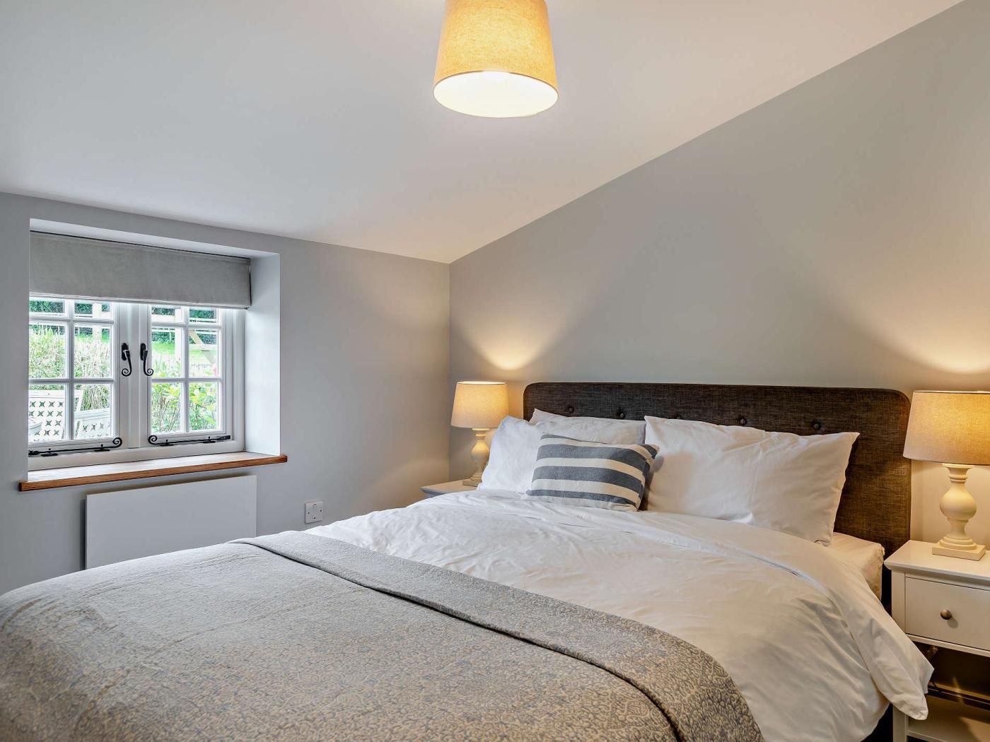 A bedroom with a bed, bedside lamps, a window with curtains, and a ceiling light fixture.