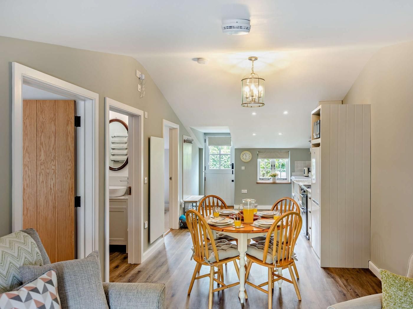 A modern kitchen with a dining area, wooden flooring, and a visible clock on the wall.