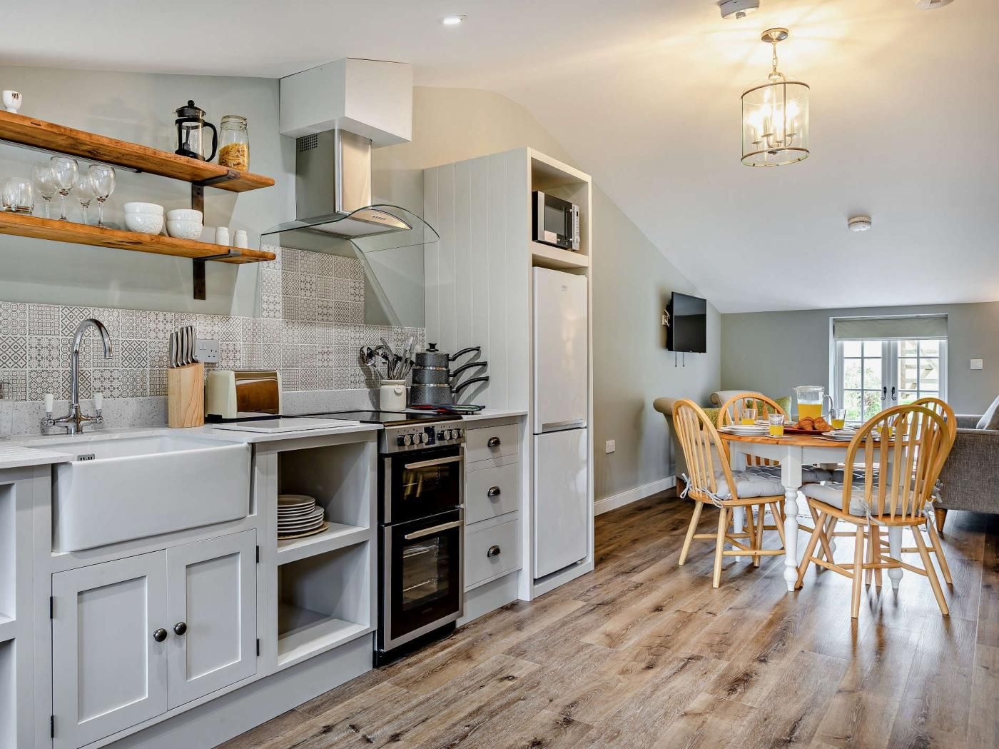 A modern kitchen with a dining area, wooden flooring, and a TV mounted on the wall.