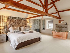 A bedroom with a large bed, a wooden ceiling, a radiator, a wall-mounted mirror, and a copper bathtub. - 3 Bed in Driffield (oc-92697) (Lund)