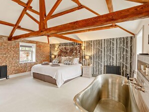 A bedroom with a large bed, a wooden ceiling, a brick wall, and a large bathtub. - 3 Bed in Driffield (oc-92697) (Lund)