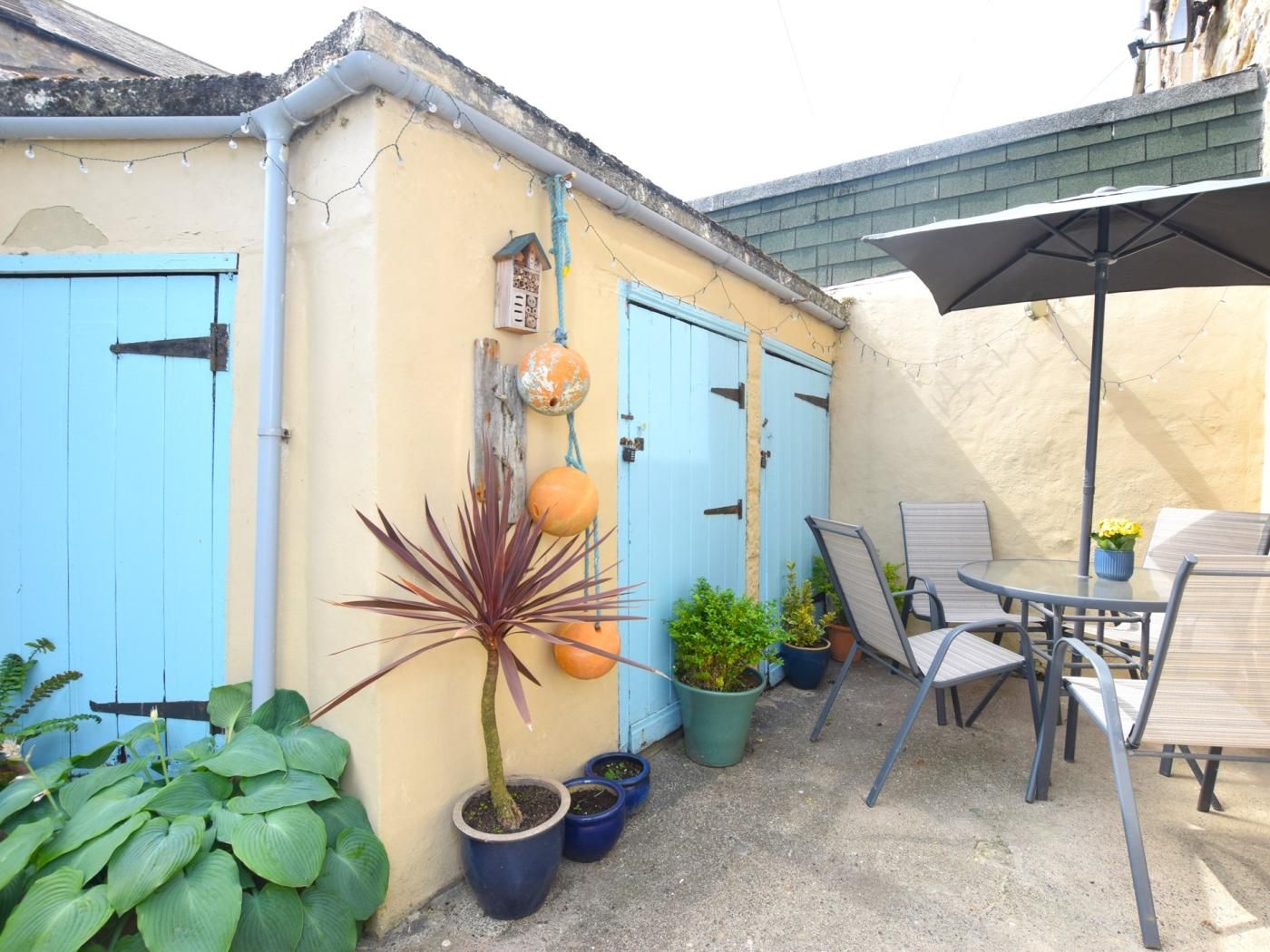 Un espace patio avec une table et des chaises, des plantes en pot et une porte bleue.