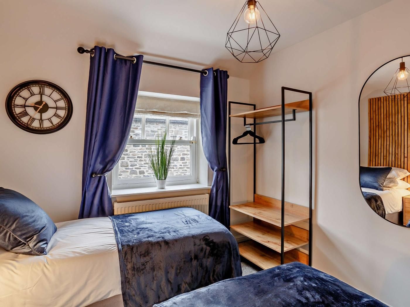 Un dormitorio con cama, ventana con cortinas, una planta, lámpara colgante y un espejo.