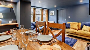 Un comedor con una mesa de madera dispuesta para una comida, un sofá con cojines y vistas a una pared de piedra a través de una ventana.