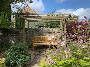 A garden with a wooden bench under a pergola, surrounded by stone walls and flowering plants. - 3 Bed in Langport (oc-75576) (Curry Rivel)