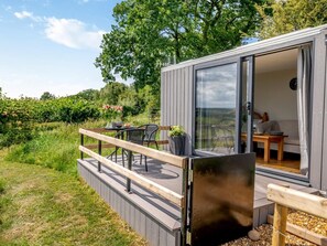 Een modern terras buiten met een tafel, stoelen, een houten balustrade en uitzicht op het omliggende landschap.