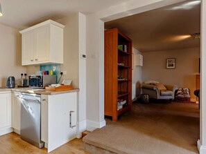 A compact living space with a kitchenette, a wooden bookshelf, a sofa, and a small dining table. - 2 Bed in Torquay (oc-82540) (Torquay)