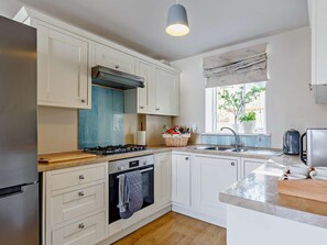 Une cuisine moderne avec des meubles blancs, une cuisinière à gaz, un four, un évier et une fenêtre donnant sur un paysage verdoyant.