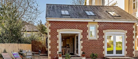 Una casa de dos pisos con fachada de ladrillo, una entrada visible y un pequeño patio con muebles de exterior y plantas en macetas.