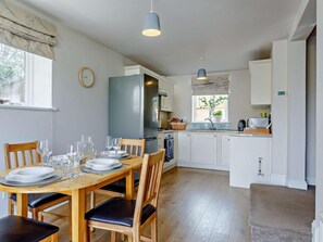 A compact kitchen with white cabinets, a built-in oven, and a dining area with a wooden table and chairs. - 2 Bed in Torquay (oc-82540) (Torquay)