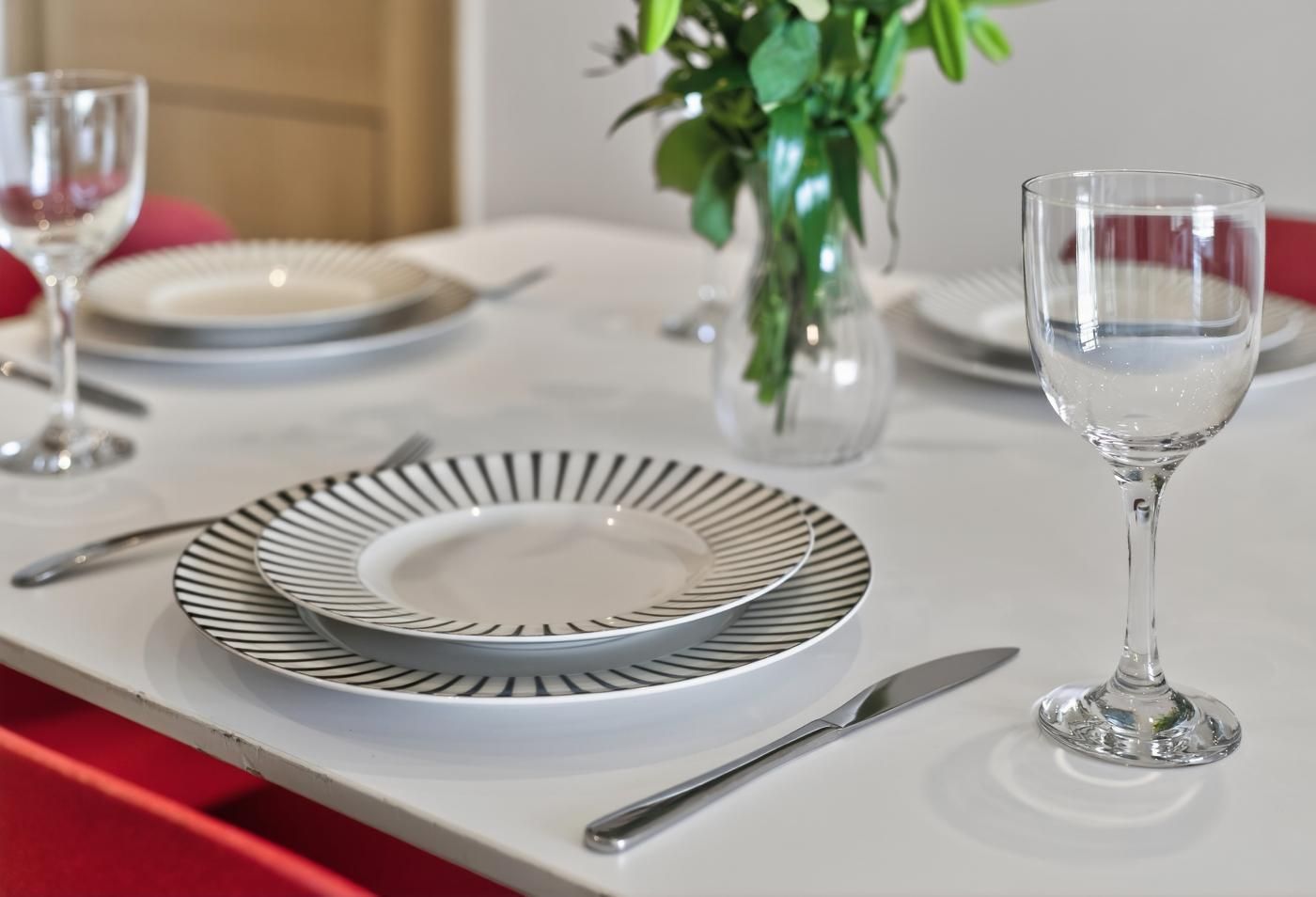 Une table à manger dressée avec des assiettes, des couverts et un verre d’eau.