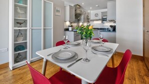 Een eetgedeelte met een witte tafel gedekt voor vier personen, rode stoelen en een keuken op de achtergrond.
