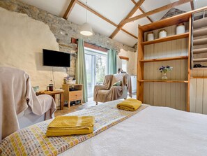 Ein gemütliches Zimmer mit einem Bett, einem Fernseher, einem Holzboden und einer Steinwand.