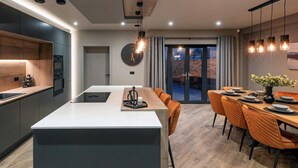 Ett modernt kök med en köksö i mitten, en matplats med ett träbord och orange stolar samt ett stort fönster med gardiner.