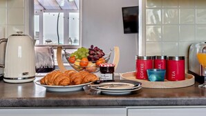 Keittiön työtasolla on kahvinkeitin, croissant-leivoksia, hedelmäkulho sekä punaisia säilytysastioita, joissa on merkinnät kahvi, tee ja mehu.